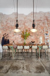 an industrial dining room with brick walls, an industrial dining table, tall metal stools, large pendant lamps on unique chains