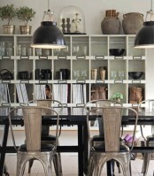 a modern industrial dining room with a white storage unit, a large black dining table, metal chairs, black metal pendant lamps and greenery