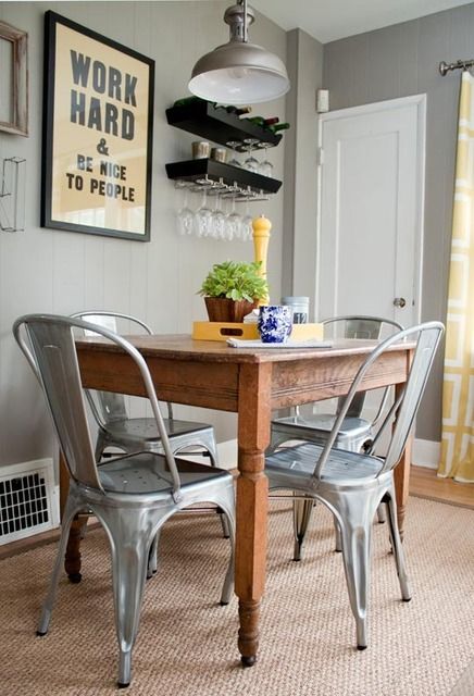 a small industrial dining room with a stained vintage table, metal chairs, a metal pendant lamp and some vintage signs