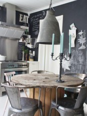 an industrial dining space with a chalkboard accent wall, a dining table made of a wooden spool and metal chairs plus a metal lampshade over the table