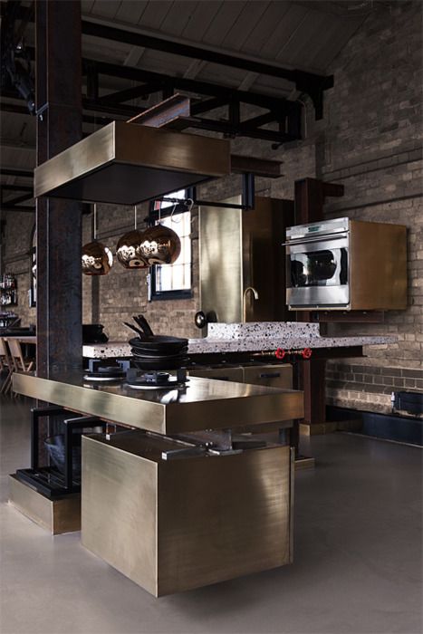 a minimalist industrial kitchen with sleek and shiny metal cabinets, a terrazzo countertop, brick walls and wall mounted appliances is super chic