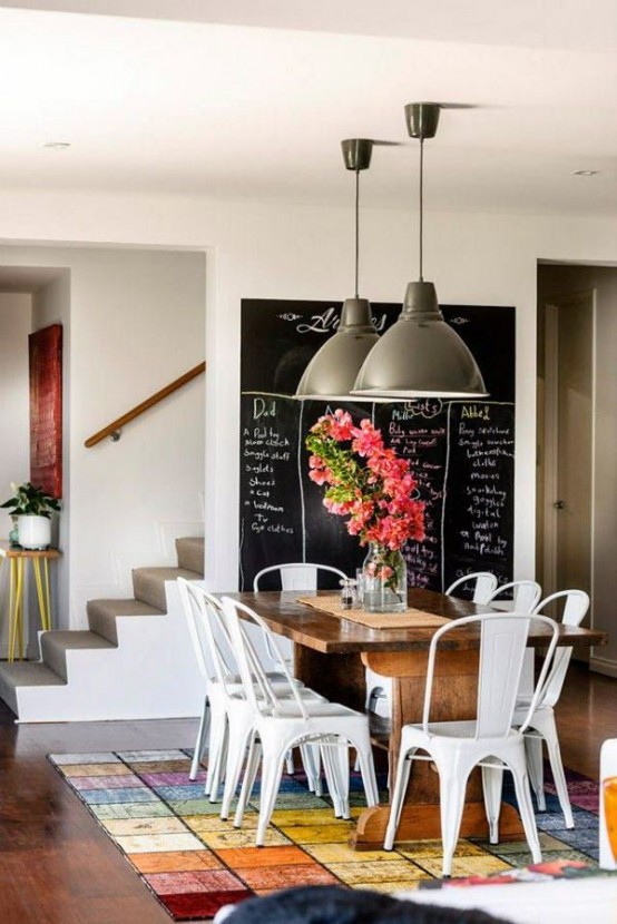 an industrial dining space with a large chalkboard, a stained table, white metal chairs and metal pendant lamps is a lovely space to have meals