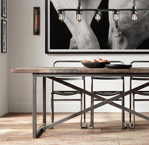 a minimalist industrial dining space with a large dining table with metal legs, minimalist metal chairs, a metal and bulb chandelier and a black and white statement photo