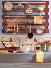 a wall-mounted pallet with railings that feature holders for all kinds of stuff, from clocks to utensils is a cool idea for a rustic space