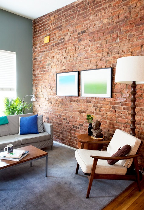 an eclectic living room with a statement red brick wall and colorful touches and artworks