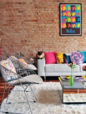 an eclectic living room with a red brick statement wall, colorful pillows and artworks