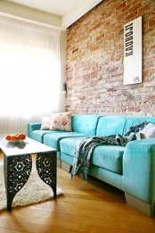 an eclectic living room with a turquoise sofa, a red brick wall and a refined coffee table