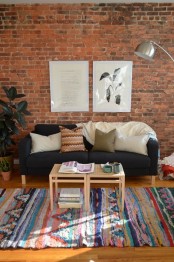 a bright boho chic living room with a red brick wall and colorful rugs and textiles