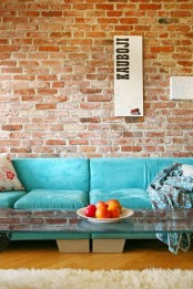 a red brick statement wall contrasts the bright turquoise sofa and a glass coffee table