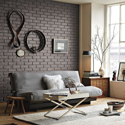 a contemporary living room with a grey brick wall and some leather and metal for an industrial touch