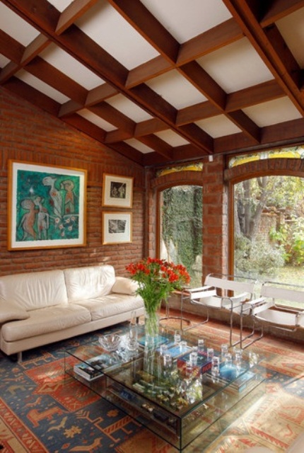 a mid-century modern living room with red brick walls, printed rugs and a coffered ceiling