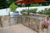 a simple and stylish outdoor kitchen built of stone and metal with a grill, a cooler and cooking coutnertops