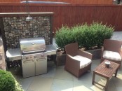 a simple outdoor bbq area with a grill, a couple of chairs and a coffee table plus greenery around