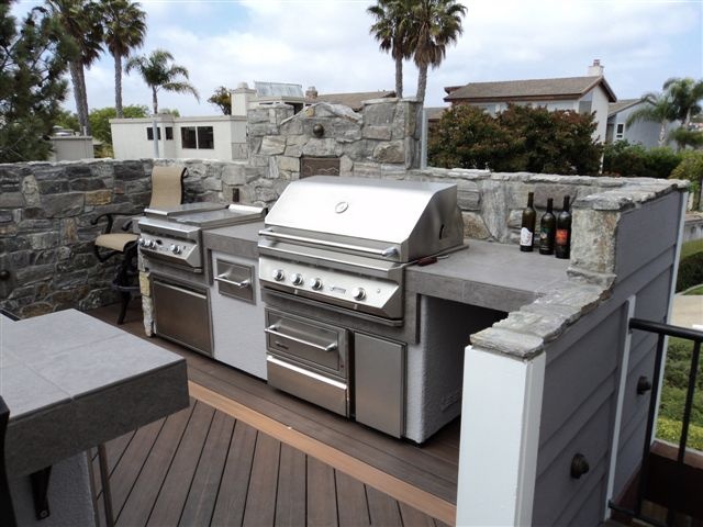 an outdoor kitchen built of stone, concrete and metal with a cooker and a grill for comfortable cooking