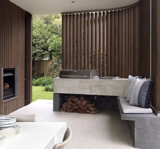 a minimalist bbq area with a concrete countertop flowing into a bench, with a grill on top and some firewood underneath