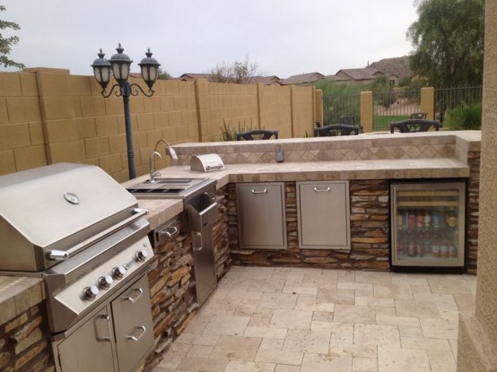 an outdoor bbq area of stone and tiles, with a cooking countertop, a sink and a grill