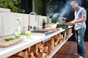 a contemporary outdoor kitchen with firewood storage, a sink, a cooking zone and a grill