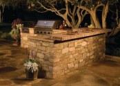 a simple outdoor kitchen clad with stone and with countertops plus a grill for cooking