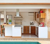 a minimalist outdoor kitchen with white cabinets and wooden doors, a hood and a grill plus an additional eating space