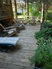 a rustic deck with wooden chairs and loungers, striped cushions and pillows and greenery around