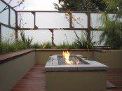 a contemporary deck with a white and wood walls for some privacy, a built-in bench, a fire pit and some grasses growing around
