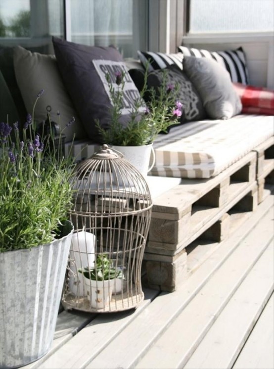 a Scandinavian deck with a pallet sofa, lots of pillows, a cage for decor and potted greenery and blooms