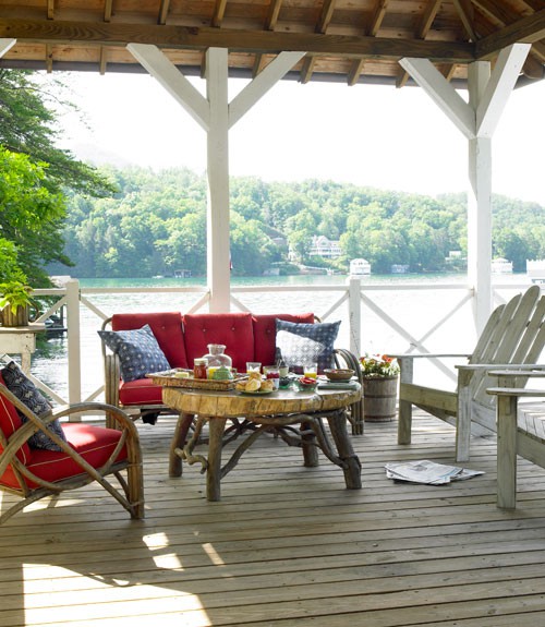 a rustic and relaxed deck with rattan and whtewashed wooden furniture, colorful textiles, a living edge table with food and drinks