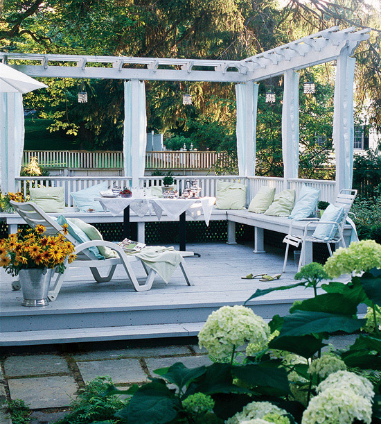 a small and cozy deck in white with a built-in bench and several loungers plus potted blooms and greenery