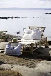 a tropical lounger made of neutral wood, with white upholstery and pillows and blankets looks dreamy and chic