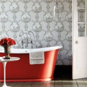 a refined bathroom with grey printed wallpaper, a red bathtub and a side coffee table with burgundy blooms