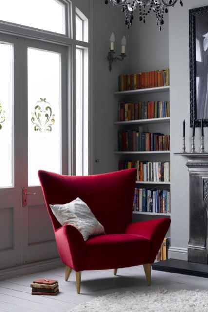 a stylish living room with grey walls and a fireplace, built in shelves with books, a deep red wingback chair and a pillow is a lovely space