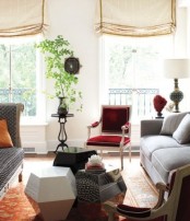 a neutral living room with grey sofas, lovely faceted coffee tables, a deep red chair, potted greenery and neutral curtains