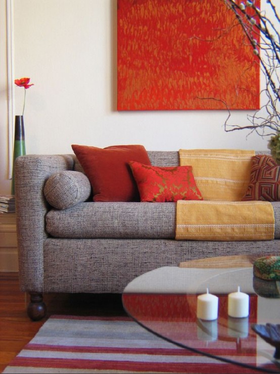 a modern living room with a grey sofa and yellow and red pillows, a bold artwork, a glass coffee table and a printed rug