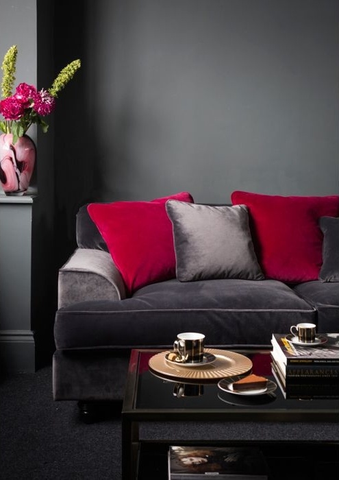 a refined moody living room with graphite grey walls, a grey sofa with red and grey pillows, a chic coffee table and bold red blooms