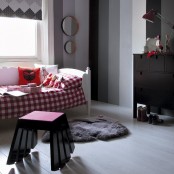 a creative kid’s room done in grey shades and red, with color block walls, a bed with red checked bedding, a catchy stool and a black dresser