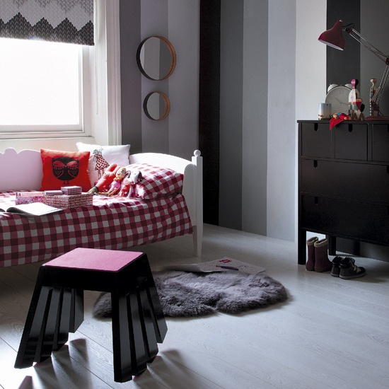 a creative kid's room done in grey shades and red, with color block walls, a bed with red checked bedding, a catchy stool and a black dresser