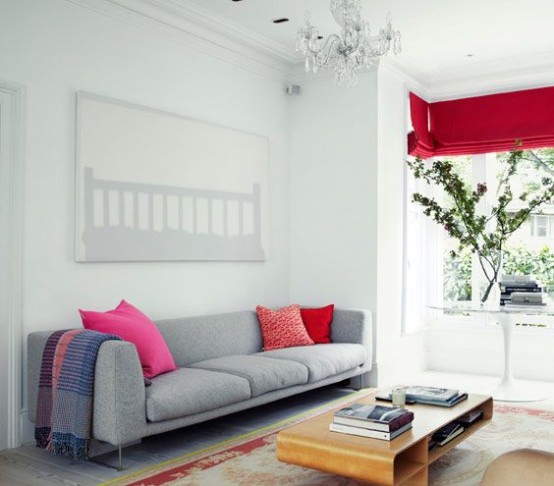 an airy living room with a grey sofa and red pillows, a red curtain, a printed rug and a small coffee table feels airy and cool