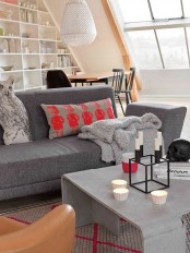 an attic living room with a shelving unit, a grey sofa and a concrete coffee table plus a grey and red pillow and a red candleholder