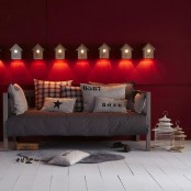 a Scandinavian living room with a red accent wall, birdhouse wall lamps, a grey sofa with red and white printed pillows and a white planked floor
