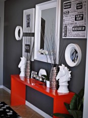a modern entryway with graphite grey walls, a gallery wall, a mirror and a red console table with beautiful decor