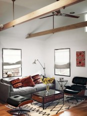 a beautiful mid-century modern living room with a grey sofa, black chairs, a chic coffee table, a printed rug and wooden beams, red pillows and an artwork