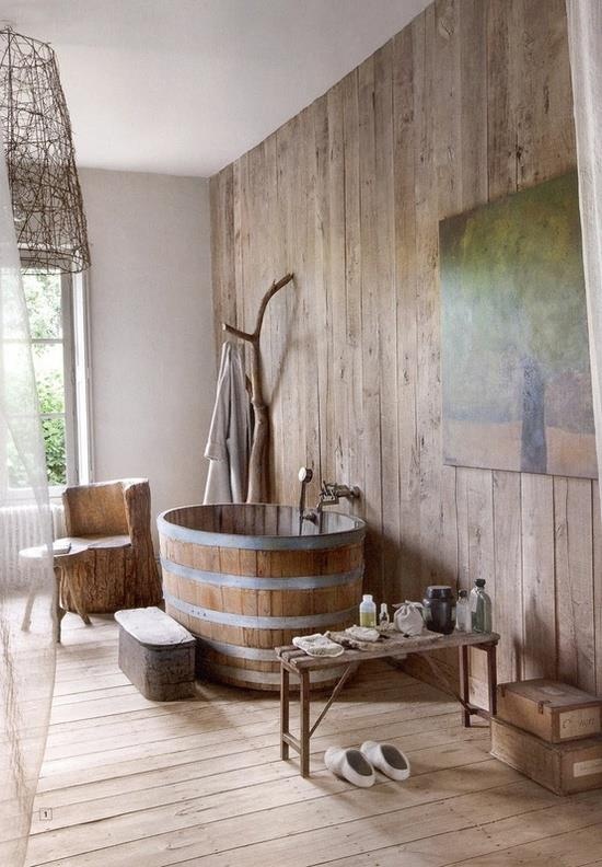 a cozy and airy rustic bathroom with much wood, a wooden tub and a trunk for hanging clothes