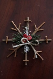 a rustic Christmas ornament of sticks, evergreens and red buttons for a cozy feel