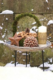 a rustic Christmas decoration of a moss wreath, a star, a large candle, nuts on a plate and a nut topiary