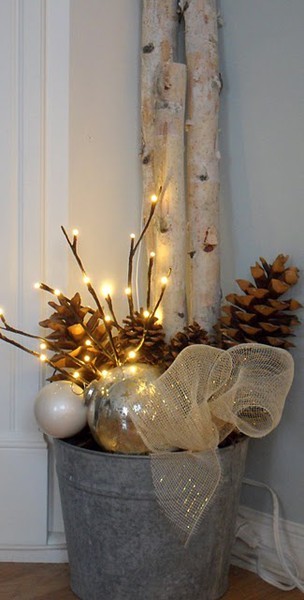 a galvanized bucket with branches, lights, pinecones, ornaments and a large bow
