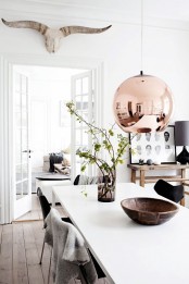 an airy Nordic dining room with a white table and mismatching chairs, a copper pendant lamp and some art and a wooden bowl