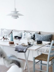 a serene and fresh Scandinavian dining space with a sleek storage bench, mismatching chairs, a simple IKEA table and lots of soft pillows and cushions