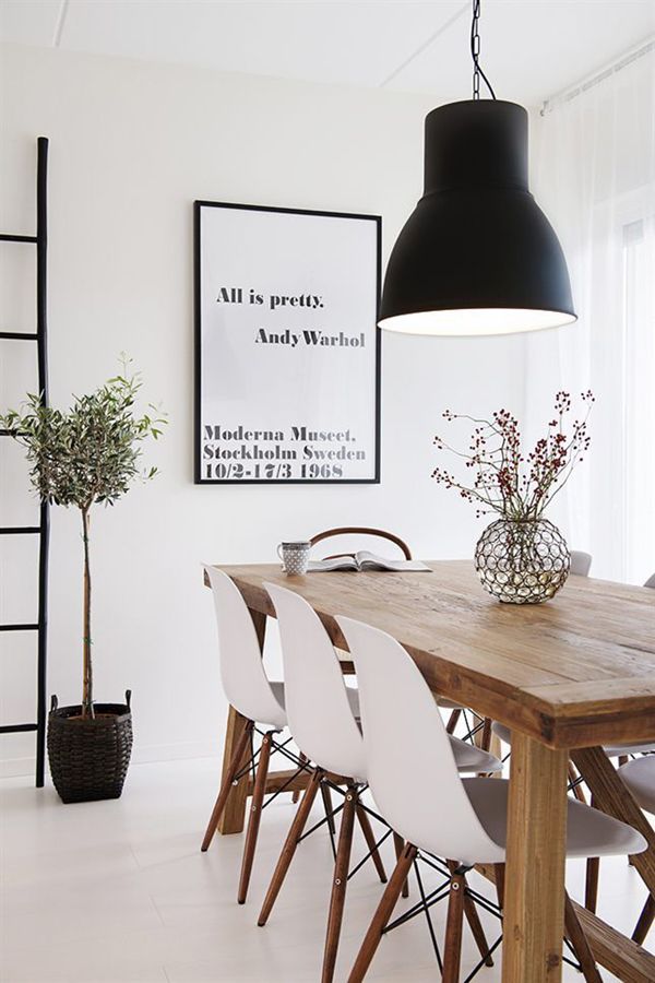 a beautiful Scandinavian dining room with a light stained wooden table, matching white chairs, a statement black pendant lamp and an artwork