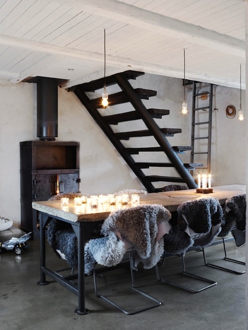 a Scandinavian dining room with a wood and metal table, matching metal chairs covered with faux fur and a vintage metal hearth plus bulbs and candles