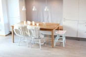 a serene Nordic dining room with a built-in wooden bench, a stained wooden table and whitewashed chairs with faux fur plus pendant lamps